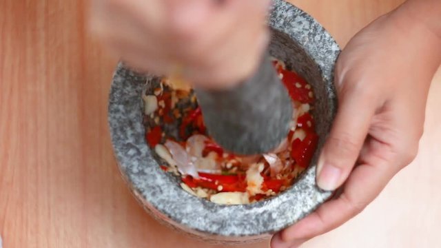 Top view hands of woman punching red hot fresh chilli and garlic with mortar stone prepare mixing herb seasoning before cooking thai food warm tone processed
