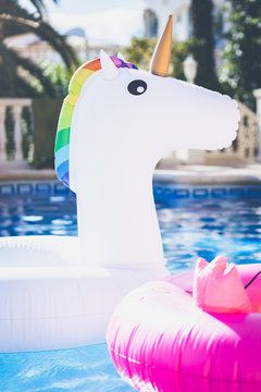 Inflatable colorful white unicorn and pink flamingo at the swim pool. Holidays time in the swimming pool with plastic toys. Relaxation and fun concept.Vertical