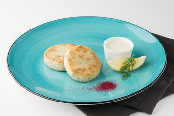 Fried ling perch cutlets with lemon, white sauce and vendure on turquoise plate and black napkin on white background