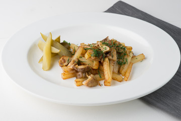 Fried potatoes with mushrooms, parsley and pickles on round plate