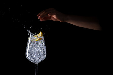 Female hand splashing lemon into the iced water on black background