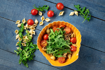 Pasta with tuna and arugula in shaped plate on wooden background. top view
