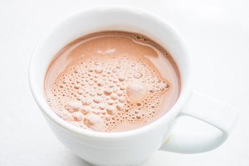 Cocoa drink with bubbles in a white mug on the table.