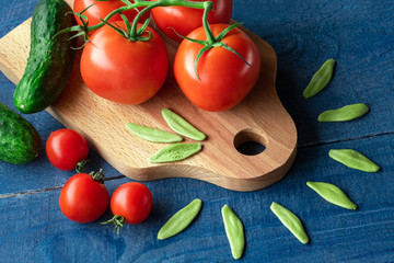 Tomatoes and cucumbers on wooden board with raw pasta on blue background