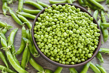 Peeled green peas in a plate on a wooden table.
