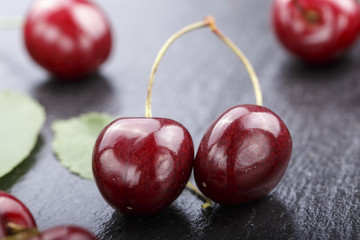 red sweet cherries and green leaves on a black slate background