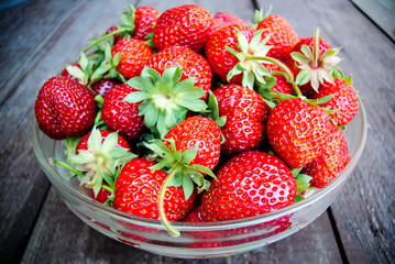 Juicy strawberries in a glass plate on a wooden background
