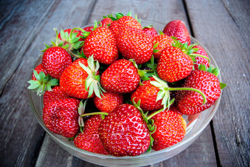 Juicy strawberries in a glass plate on a wooden background
