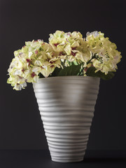 Fake flowers in a vase of white color on a black background