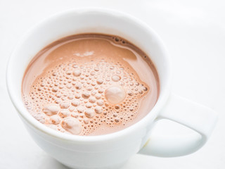 Cocoa drink with bubbles in a white mug on the table.