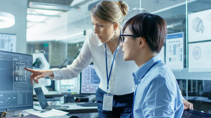Asian Scientist Sitting at His Desk Consults Senior Engineer about Sophisticated Coding and Programming. In the Background Computer Science Research Laboratory with Robotic Arm Model. © Gorodenkoff