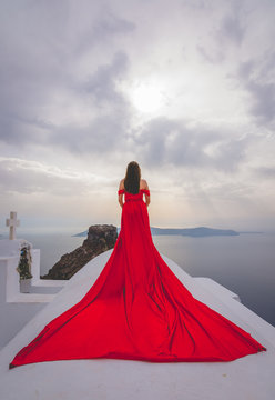 Elegante Chica Con Vestido Rojo Posando En El Techo De Una Casa Blanca En La Isla De Santorini.