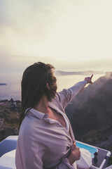 Chica enseñando hacia la puesta del sol en Imerovigli, Santorini