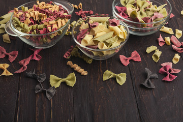 Various colorful pasta in glass bowls on wooden background