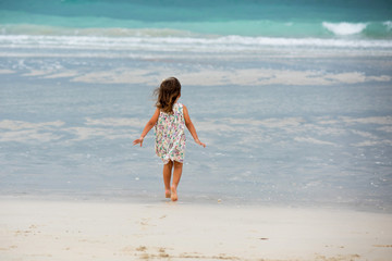 Fototapeta na wymiar Little girl runs on the beach and wear beautiful dress in cloudy day in Dubai