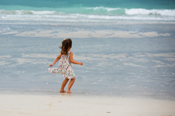 Fototapeta na wymiar Little girl runs on the beach and wear beautiful dress in cloudy day in Dubai