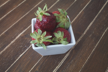 strawberries inside white bowl on a wooden table viewed from close up