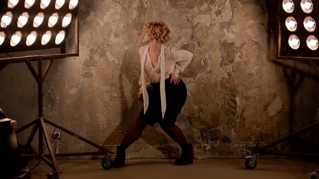 Young female blonde caucasian dancer dancing in front of studio light. Overall plan.