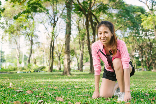 Asian young woman on mark to set ready for jogging exercise to buld up her body on glass in warm light morning. Young woman do exercise workout in park to make body beauty. Outdoor jogging in the park