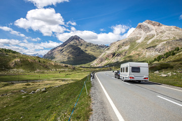 A caravan on the way to the vacations. Swiss mountains with a cloudy sky. Beautiful camping holidays with a camping car. Family travel in Europe. 