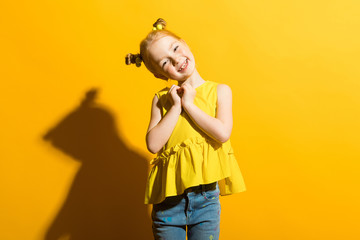 Girl with red hair on a yellow background. The girl clasped her heart.