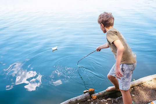 Boy plays with paper boat and launches it on the lake