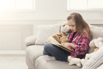 Obraz premium Happy little child reading book for her teddy bear