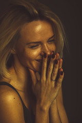 Blonde woman laughs, closing her smile with her hands