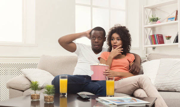 Surprised black young couple watching TV at home