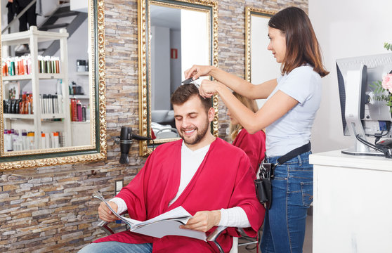 Young female hairdresser cuts hair of young man client  at salon
