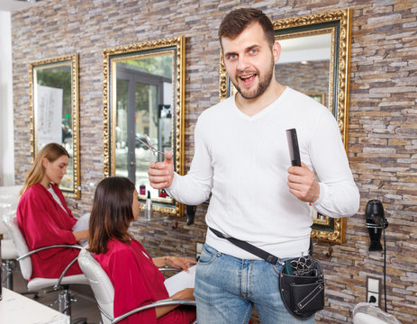 Male hairdresser  standing in beauty studio, clients on background