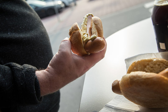 Mann isst Bockwurst im Brötchen als schneller Snack auf Parkplatz