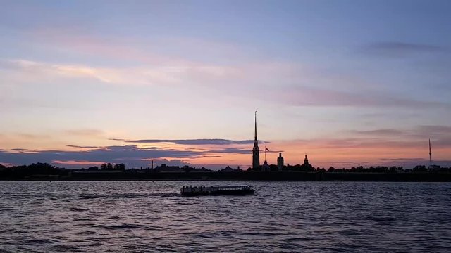 White nights in St. Petersburg. Historic centre. The ship floats on the Neva river. Silhouette of the Peter and Paul fortress against the purple sunset. A romantic evening in a beautiful city