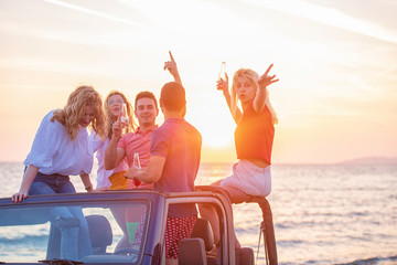 Five young people having fun in convertible car at the beach at sunset.