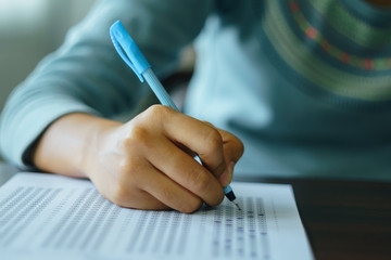 Close up of student's hand holds a pen write on answer sheet. Student answers multiple choice...
