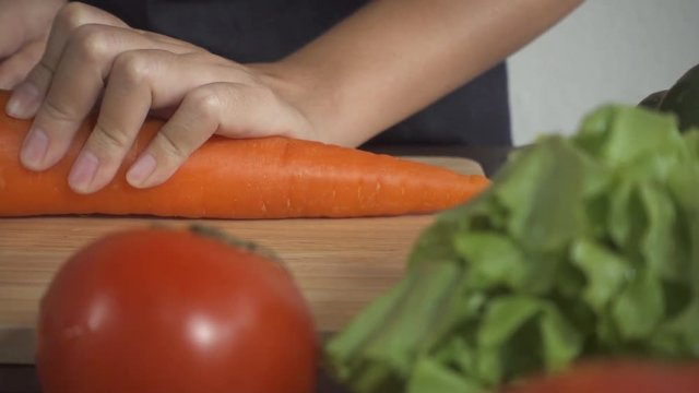 Slow motion - Close up of woman making healthy food and chopping carrot on cutting board in the kitchen.