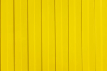 A corrugated fence of yellow metal sheets with screw. Texture of metal fence