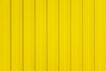 A corrugated fence of yellow metal sheets with screw. Texture of metal fence