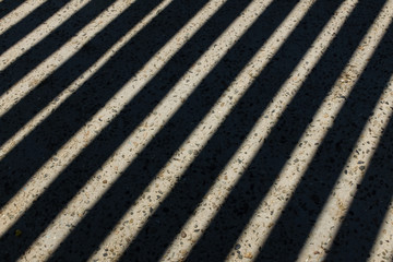 Sunlight shines through wooden fence and makes geometric stripes shadows on the ground. Shadows of wooden fence on the ground. Fence shadows texture
