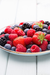 Fresh berry salad on blue dishes. Vintage wooden background.