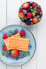Fresh berry salad on blue dishes. Vintage wooden background.