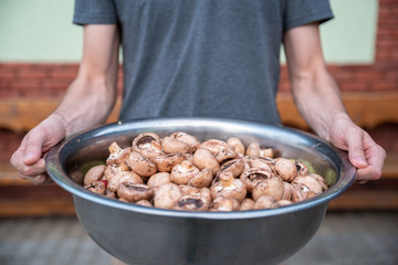 Man holds a bowl filled with fresh champignon mushrooms, preparation for cooking