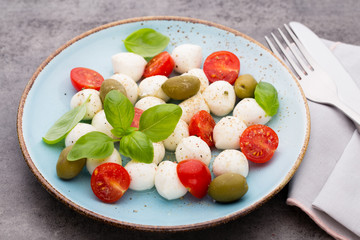 Delicious caprese salad with ripe cherry tomatoes and mini mozzarella cheese balls with fresh basil leaves.