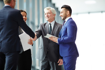 One of colleagues shaking hands with foreign businessman after discussion of working moments