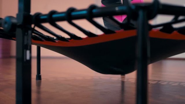 Bottom View to Lady's Feet in Sneakers Jumping on Mini Trampoline during Fitness Class in the Sport Gym. Nice Slow Motion in 4K