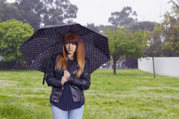 Redhead woman with a black umbrella. Standing at the rain in beautiful spring park.