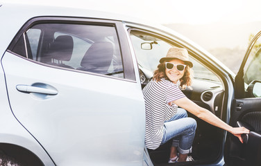 Young beautiful female travel girl in hat and sunglasses speaks by mobile phone on the background of her car while traveling in the mountains, renting and car service
