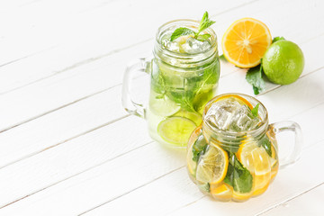 Two glass glasses with homemade lemonade from lime and lemon, sliced citrus on a white wooden rustic background. Copy space