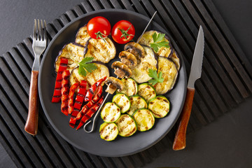 Grilled vegetables: eggplant, zucchini, pepper. Skewer with mushrooms. On a black plate and a black background. Toned.