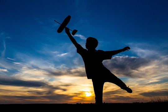 Silhouette of boy with his airplane against sunset